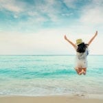 Happy young woman in casual style fashion and straw hat jumping at sand beach. Relaxing, fun, and enjoy holiday at tropical paradise beach with blue sky and white clouds. Girl in summer vacation.